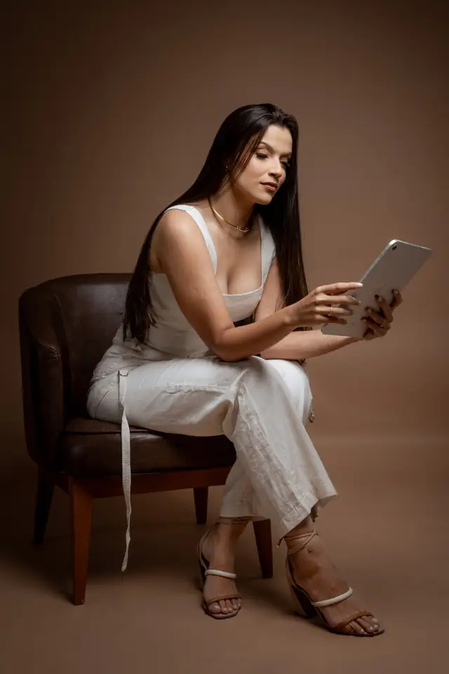 Jullya Fonseca sentada em uma poltrona, analisando conteúdo no tablet